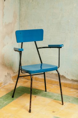 blue chair inside an old room with yellow and greem floor