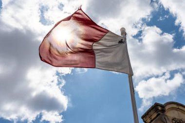 Ulusal Malta bayrağı güneşin önünde rüzgarda sallanıyor.