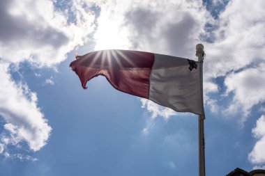 Ulusal Malta bayrağı güneşin önünde rüzgarda sallanıyor.