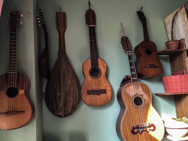 Yeşil duvarda asılı gitarlar, farklı boyutlarda, ve biraz güneş ışığı.