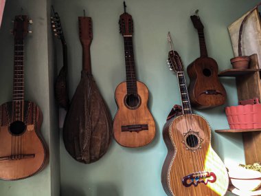 Yeşil duvarda asılı gitarlar, farklı boyutlarda, ve biraz güneş ışığı.