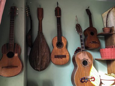 Yeşil duvarda asılı gitarlar, farklı boyutlarda, ve biraz güneş ışığı.