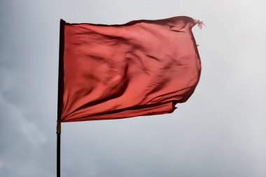 Gökyüzüne karşı rüzgarda kırmızı bir bayrak beliriyor..