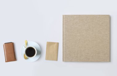 Masanın üzerinde bir fincan kahvenin olduğu büyük bir bej kaplı defter var.