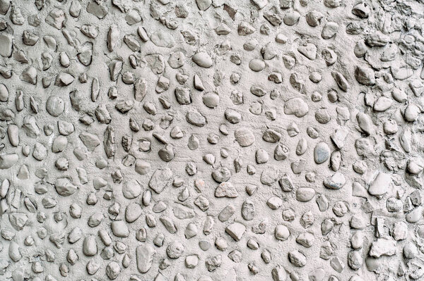 Gray cement wall with round stones close up.