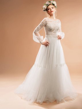 Beyaz gelinlik ve çiçekli çelenk içinde bej arka planda beyaz bir stüdyoda beyaz bir gelin.