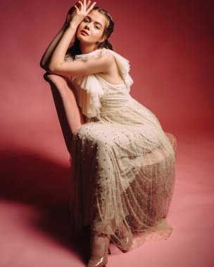 Somon arka planında fildişinden yapılmış pohpohlayıcı elbisesi olan güzel esmer kadın. Kırmızı stüdyo odasında soluk pembe koltuklu muhteşem gelin. Moda çekimi..