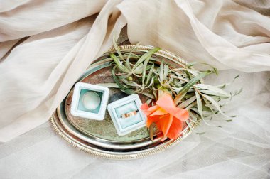 Altın alyanslar. Nikâh yüzüğü, nişan yüzüğü, taze portakal çiçeği, yeşil yapraklar, gümüş tepsi ve toz grisi bezin düz kompozisyonu. Sonsuz aşk kavramı.