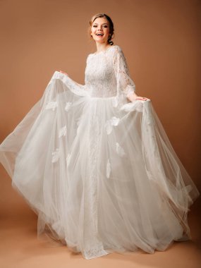 Gülümseyen mutlu bir gelin ve stüdyoda yürüyen uzun beyaz bir gelinlik. Gelinlik modası. Altın arkaplan ile tam boy portre. 