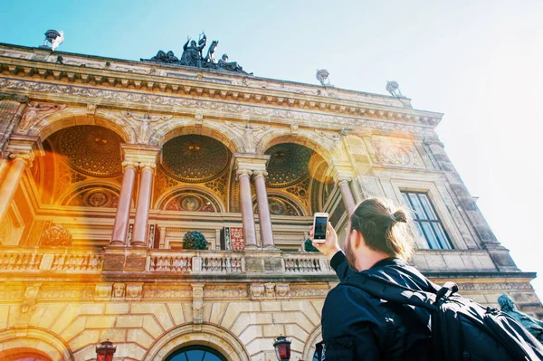 Travel concept. Man with a bun photographs on the mobile phone a beautiful building in a European city.