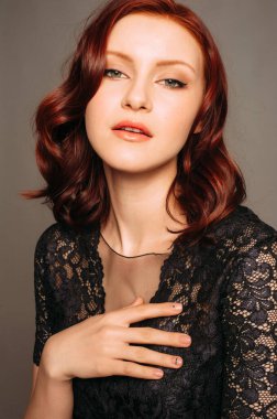Gri arka planda siyah dantel bluzlu güzel kızıl bir kadının stüdyo portresi. Küçük siyah bir elbisenin içinde şenlikli şehvetli bir görünüm. Doğal makyaj ve saç kesimi..