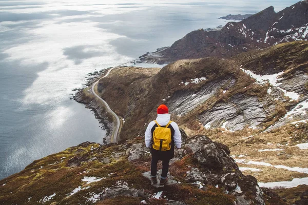 Hombre viajero con una mochila amarilla con un sombrero rojo de pie sobre el fondo de las montañas y el mar. Concepto de estilo de vida. Dispara por la espalda — Foto de Stock