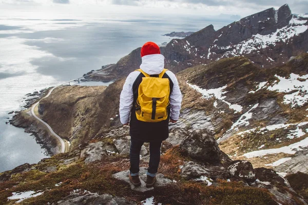 Hombre viajero con una mochila amarilla con un sombrero rojo de pie sobre el fondo de las montañas y el mar. Concepto de estilo de vida. Dispara por la espalda — Foto de Stock