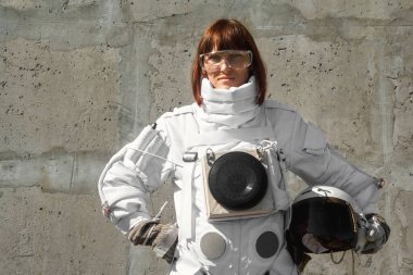 Gri bir duvarın arkasında kaskı olmayan güzel bir astronot kız. Fantastik uzay giysisi.