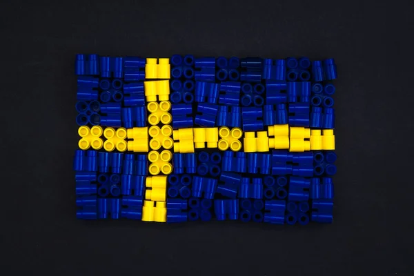 Färgglada plasttegelstenar som bildar Sveriges flagga på svart papper bakgrund. Delar till ljusa små reservdelar till leksaker. Ovanifrån. — Stockfoto