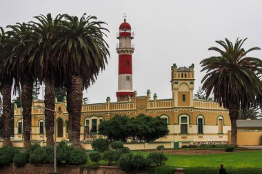 Swakopmund, Namibya - 12 Temmuz 2019: Kızıl deniz feneri, beyaz Alman kalesi ve Namibya 'nın sömürge kasabası Swakopmund' daki sıra sıra palmiye ağaçları