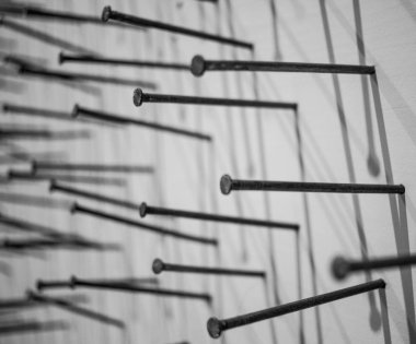 Yapı çivilerinin siyah ve beyaz bir fotoğrafı tuvale sokuluyor ve üzerine gölge düşürülüyor. Yapı çivilerinin makro fotoğrafçılığı beyaz arka plan çivilerine siyah inşaat çivileri çakmak beyaz arka plan üzerine bir arka plan oluşturur. beyaz boya