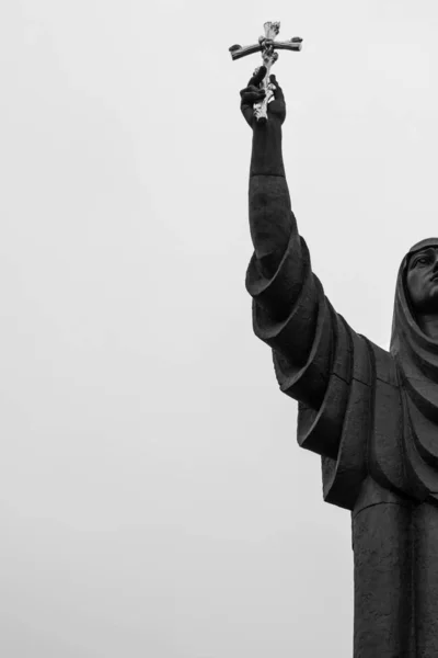 religious statue of a woman holding an Orthodox cross in her hand. faith. statue against the sky. Orthodox cross against the sky.