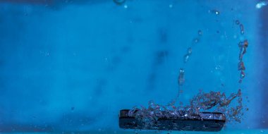 Siyah beyaz telefon suya düştü. Telefonun suda. Mavi su. Telefon su kabarcıklarında. Telefon suya batıyor.