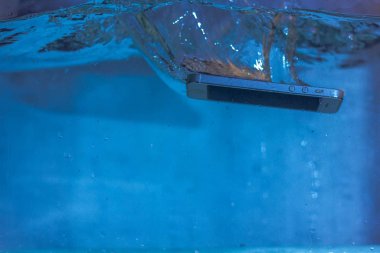 Siyah beyaz telefon suya düştü. Telefonun suda. Mavi su. Telefon su kabarcıklarında. Telefon suya batıyor.