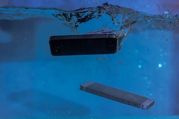 black and white phone dropped into the water. phone in water. blue water. phone in water bubbles.phone sinks in water