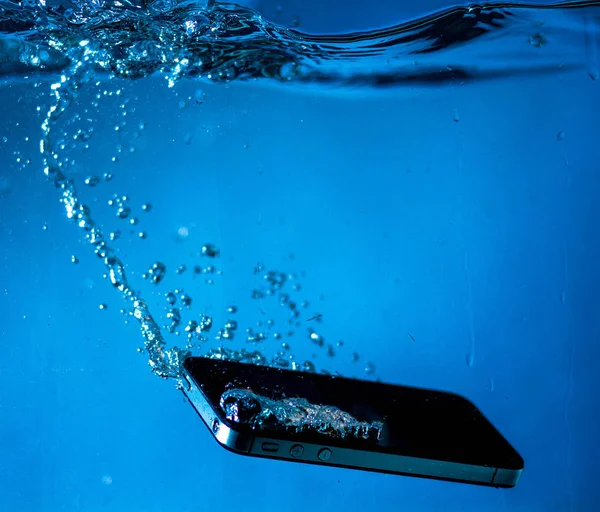 black and white phone dropped into the water. phone in water. blue water. phone in water bubbles.phone sinks in water