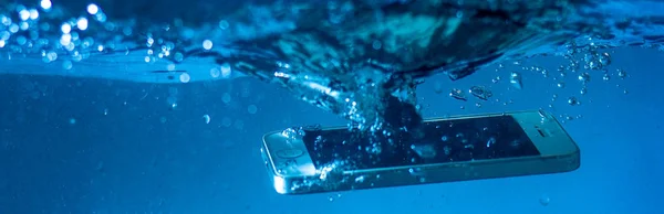 black and white phone dropped into the water. phone in water. blue water. phone in water bubbles.phone sinks in water