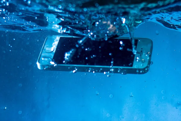 black and white phone dropped into the water. phone in water. blue water. phone in water bubbles.phone sinks in water