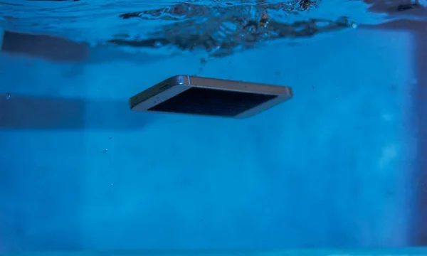 black and white phone dropped into the water. phone in water. blue water. phone in water bubbles.phone sinks in water