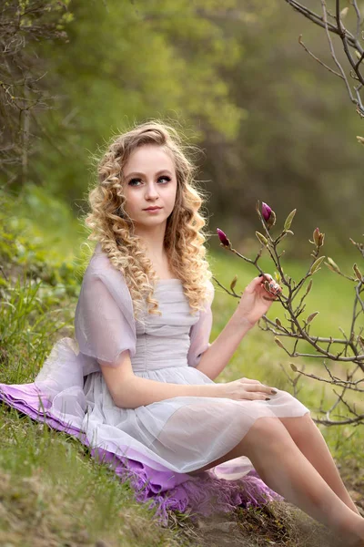 Joven hermosa chica en un vestido lila luz en el jardín donde —  Fotos de Stock