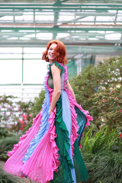 Hermosa chica pelirroja en arreglista donde azalea florece en un vestido volador colorido — Foto de Stock