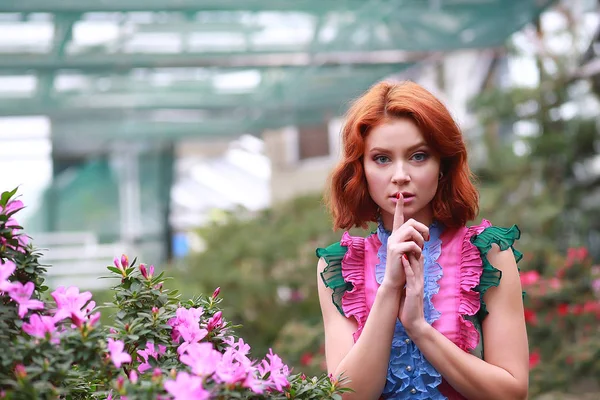Красива руда дівчина в аранжувальнику, де цвіте лазалія в барвистій літаючій сукні — стокове фото