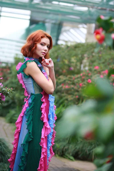 Hermosa chica pelirroja en arreglista donde azalea florece en un vestido volador colorido — Foto de Stock
