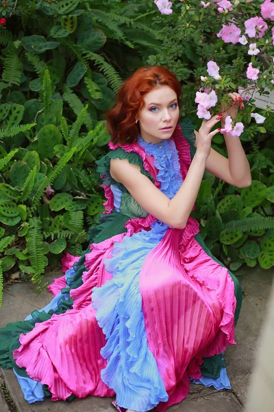 Mooi roodharig meisje in arrangeur waar azalea bloeit in een kleurrijke vliegende jurk — Stockfoto