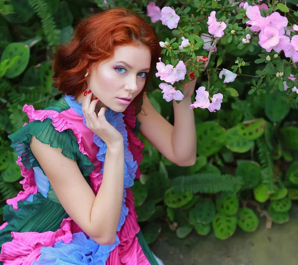 Hermosa chica pelirroja en arreglista donde azalea florece en un vestido volador colorido —  Fotos de Stock