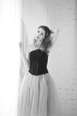 Mor tüllü etekli, siyah korseli güzel kızıl saçlı kız pencerenin yanında duruyor.