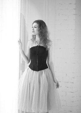 Mor tüllü etekli, siyah korseli güzel kızıl saçlı kız pencerenin yanında duruyor.