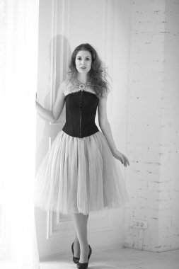 Mor tüllü etekli, siyah korseli güzel kızıl saçlı kız pencerenin yanında duruyor.