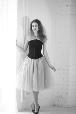 Mor tüllü etekli, siyah korseli güzel kızıl saçlı kız pencerenin yanında duruyor.