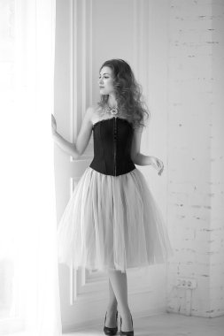 Mor tüllü etekli, siyah korseli güzel kızıl saçlı kız pencerenin yanında duruyor.