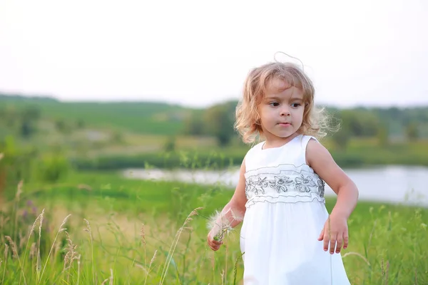 Petite fille dans un champ vert avec un gros pissenlit sur le fond du lac — Photo