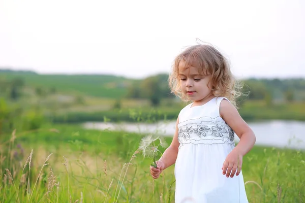 Petite fille dans un champ vert avec un gros pissenlit sur le fond du lac — Photo