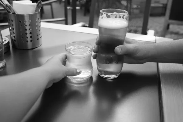Um copo de água e cerveja nas mãos de um casal em uma mesa — Fotografia de Stock