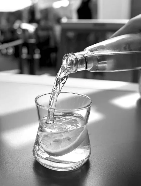 El agua mineral se vierte en un vaso sobre una mesa en un café — Foto de Stock