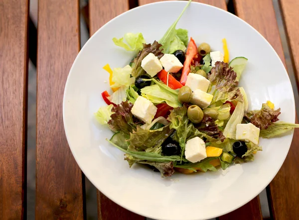 Grekisk sallad (sallad, tomater, fetaost, gurkor, svarta oliver) på en mörk trä bakgrund ovanifrån. Utrymme för text. Hälsosam mat. — Stockfoto