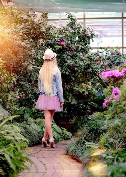 Jeune fille avec de longs cheveux blancs dans un chapeau et une veste en jean marche dans le jardin — Photo