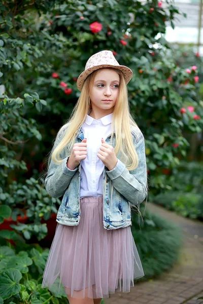 Muchacha joven con el pelo blanco largo en un sombrero y una chaqueta de mezclilla camina en el jardín —  Fotos de Stock