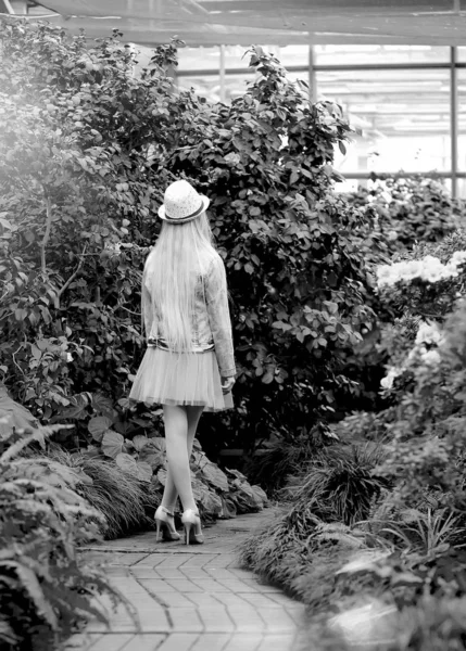 Menina com cabelos brancos longos em uma jaqueta de ganga caminha em um jardim florido — Fotografia de Stock