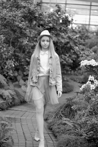 Chica con el pelo largo y blanco en una chaqueta de mezclilla camina en un jardín con flores — Foto de Stock