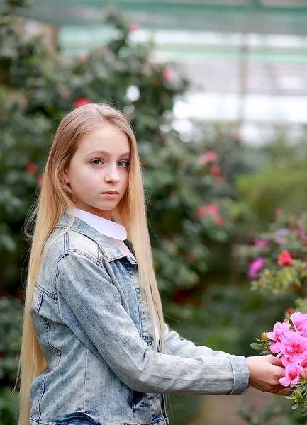 Meisje met lang wit haar in een spijkerjasje loopt in een bloeiende — Stockfoto